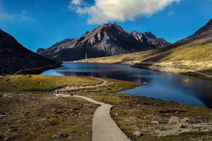 Scenic walking trail along a serene blue lake surrounded by mountains in Ziro Valley, Arunachal Pradesh.