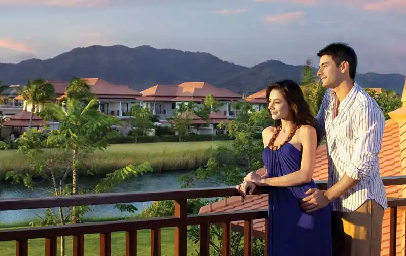 Couple standing on a resort balcony overlooking a scenic river and hill landscape in Bekal, Kerala.